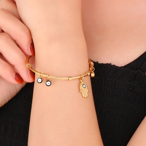 Detail of 18K gold stainless steel evil eye and hand of Fatima charms on wire cuff bracelet