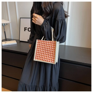 Detail of a square checkered jute tote bag with rope handles held by a model