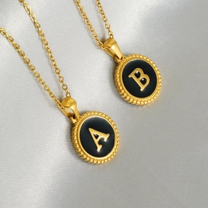 Gold plated initial A and B pendants on titanium steel necklaces over grey silk fabric