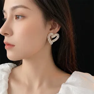 Elegant hollow heart-shaped earrings with zircons shown on a model with black background