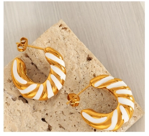 Macro detail of twisted gold and white C-shape earrings on a textured stone surface