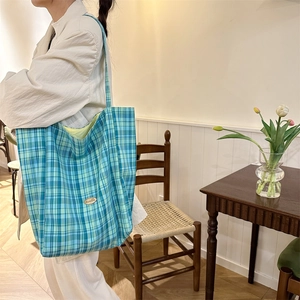 Detail of blue-green checkered tote bag featuring yellow lining and oval logo plaque