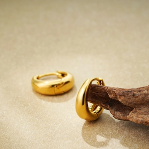 Detail view of 18K gold plated thick hoop earrings on a natural wood and stone backdrop