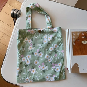 Detail of floral canvas tote bag featuring green fabric and golden metal snap fastener