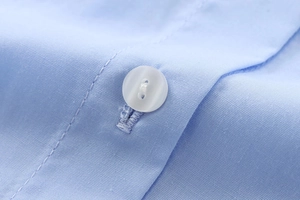 Gros plan sur une chemise en coton bleu clair avec coutures précises et bouton de qualité