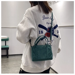 Model wearing dark green corduroy Boston bag with adjustable strap and top handles