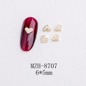 Macro shot of 6x5mm gold heart nail charms with white pearls on red manicured nail