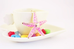 Detailed view of pink enamel starfish keychain hanging on a white porcelain coffee cup
