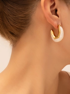 Detail of elegant gold metal and cream resin earring shown on a model's ear
