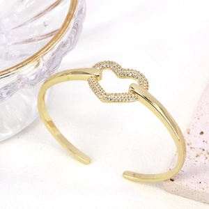 Dettaglio macro del bracciale rigido dorato con ciondolo a cuore e zirconi bianchi luminosi