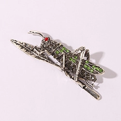 Detailed view of silver grasshopper brooch with green crystals and red gemstone eyes