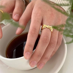 Golden bow-shaped ring shown elegantly on a finger holding a white coffee cup
