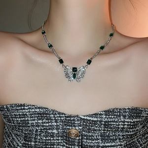 Détail macro du collier argenté avec cristaux émeraude et pendentif papillon au cou
