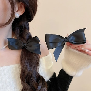 Paire de barrettes à nœuds en satin noir avec perles montrées sur cheveux tressés et en main