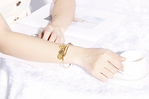 Close-up of gold Leo zodiac bracelet with lion head and symbol charms on a wrist