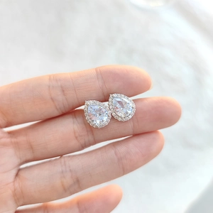 Elegant silver teardrop cubic zirconia halo stud earrings shown on finger for scale