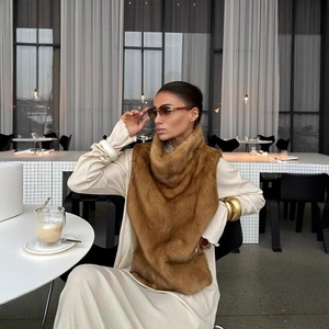 Gilet in ecopelliccia marrone con collo alto abbinato a un abito crema in un caffè