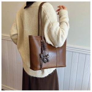 Brown leather tote bag with white stitching and cute cat charm shown on model