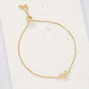Close-up of heart-shaped charm with white zircons and adjustable slider on gold chain