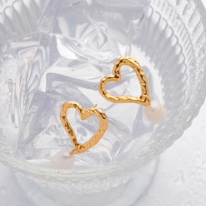 Artistic detail of gold heart earrings with freshwater pearls placed in ice water