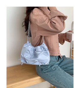 Close-up of light blue pleated shoulder bag with 3D bows and silver chain strap