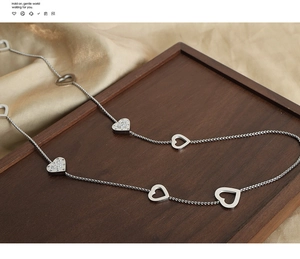 Detail of silver heart necklace with zircon pendants on walnut wood and silk background