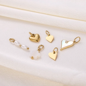Detailed view of six gold heart pendants with pearls and shell inlays on white fabric