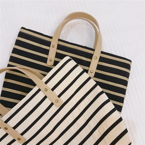 Detail of striped canvas tote bags with leather handles and reinforced metal rivets