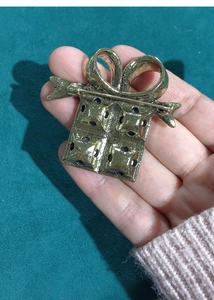 Detailed view of a gold gift box brooch with black dots and a textured bow finish