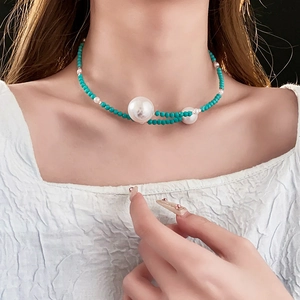 Detail of beaded turquoise necklace with white pearls worn on a textured white top