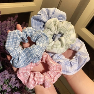 Set of five floral checkered scrunchies in pastel colors held by hand for hair styling
