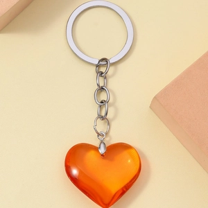 Translucent orange 3D resin heart keychain with silver metal ring on a beige background