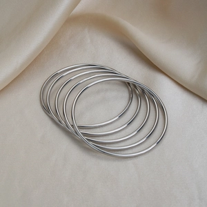 Detailed close-up of a five-piece set of polished silver minimalist bangles on silk
