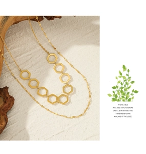 Detail of double-layer gold geometric necklace with hexagonal links on a wooden prop