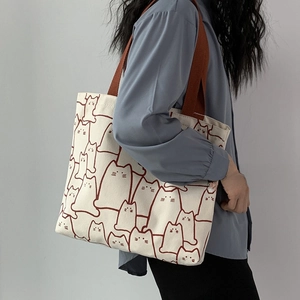 Detail of canvas tote bag featuring red cat line art and durable brown shoulder straps