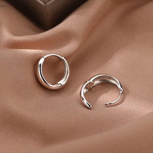Minimalist silver hoop earrings with clasp closure on champagne silk background