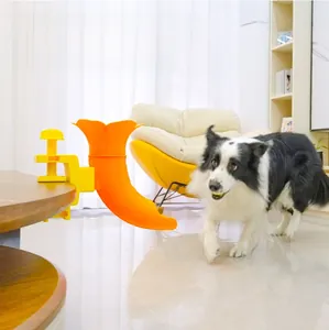 Interactive orange and yellow pet food dispenser toy clamped to a wooden table edge