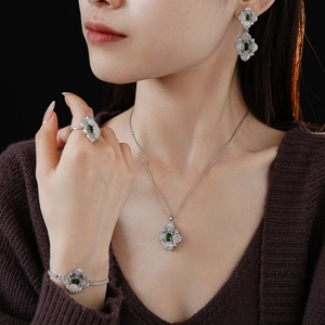 Macro shot of silver jewelry set with green gemstones worn by model against dark backdrop