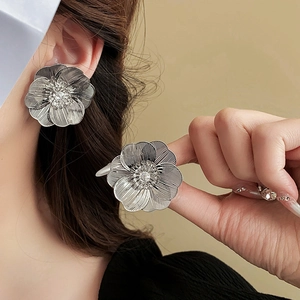 Detailed close-up of large hollow flower earrings with a clear center gemstone