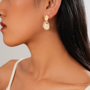 Golden earrings with square zircon and opal stones shown on model in a side profile view