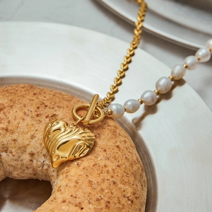 Detail of 18K gold heart pendant with liquid texture and pearl stitching chain