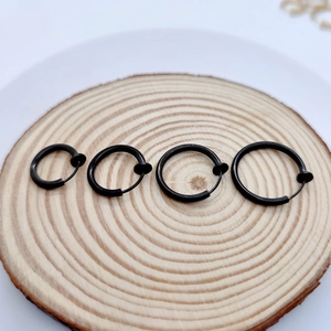 Macro view of four black clip-on hoop earrings in varying sizes on a wooden surface