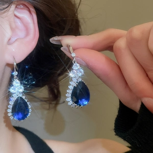 Close-up of blue teardrop crystal earrings with cubic zirconia halo on model