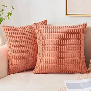 Close-up of two coral pink corduroy pillow covers on a beige sofa in a cozy room