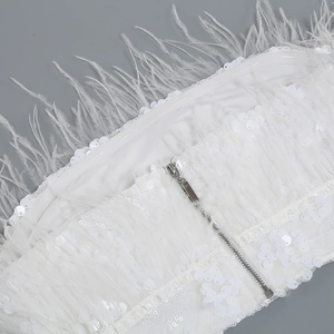 Close-up of white ostrich feathers and shimmering sequins with a silver metal zipper