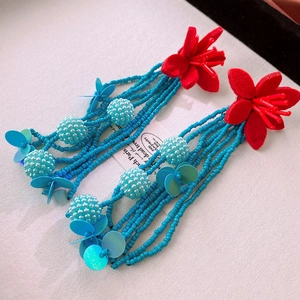 Macro detail of bohemian fringe earrings with red fabric flowers and turquoise bead tassels