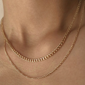Close-up of a layered gold-plated necklace set featuring a curb chain and a figaro chain