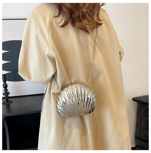 Detail of silver shell clutch bag with metallic finish and thin chain on beige coat