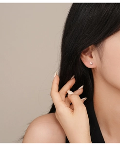 Detailed close-up of a s925 silver five-petal flower earring with colored zircon on ear