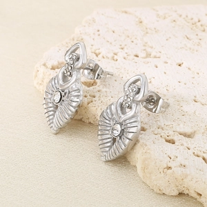Detail of silver leaf-shaped earrings with rhinestones on a beige stone texture